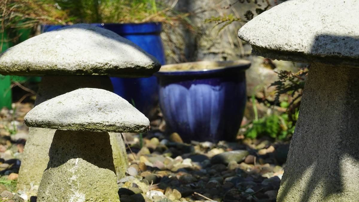 decorative outdoor garden ornaments including stone statues and metal wind spinners arranged along a garden path